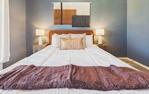 Ein Bett mit weißer Daunendecke, zwei Nachttischlampen, einem Kopfteil und einer Wandstickerei.