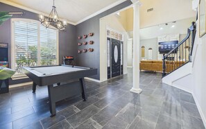 Een pooltafel in een ruime kamer met een modern design, een trap die naar een hoger niveau leidt, en een groot raam dat voor natuurlijk licht zorgt.