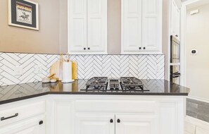 A kitchen with white cabinets, a gas stove, and a herringbone tile backsplash.