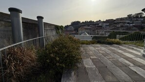 Una terraza en la azotea con barandilla de metal, suelo de hormigón y vistas a un paisaje urbano de fondo.