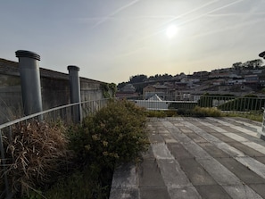 Une terrasse sur le toit, dotée d’une rambarde en métal, d’un sol en béton et offrant une vue sur le paysage urbain en arrière-plan.