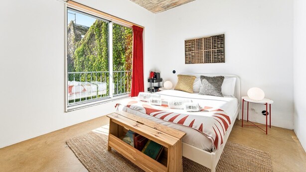 A modern bedroom with a large window, a bed with a white headboard, a bedside table, and a small side table with a lamp. - GuestReady - House of Many Faces - Room 2 (Porto)