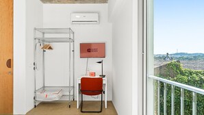Habitación de hotel con un perchero metálico, una silla roja, un televisor de pantalla plana y vistas a la ciudad.