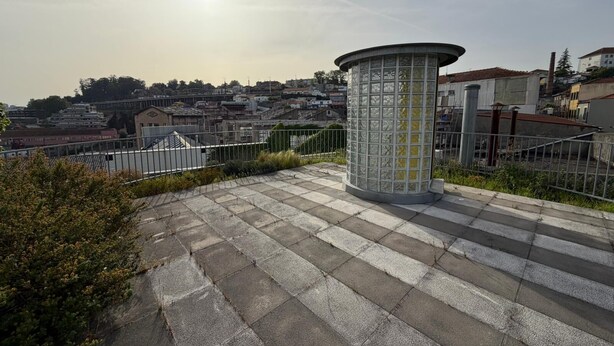 Un espacio pavimentado con una estructura cilíndrica, posiblemente un quiosco o monumento, rodeado por una cerca de metal.