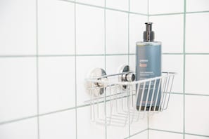 Une salle de bain avec un mur recouvert de carreaux blancs et un porte-savon métallique contenant une bouteille de shampoing.