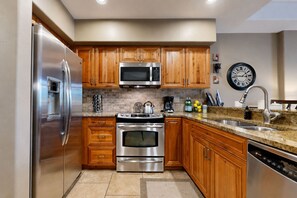 A modern kitchen with stainless steel appliances, wooden cabinets, a microwave, and a clock on the wall. - Crystal Peak Lodge 7008 ~ Ski-in/Ski-out ~ NEW LISTING ~ (Breckenridge)