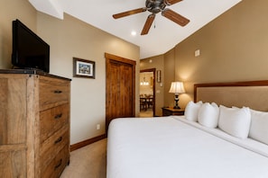 Habitación de hotel con cama, cómoda de madera, ventilador de techo y televisor sobre la cómoda.