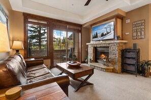 A living room with a fireplace, a sofa, a coffee table, and a television mounted above the fireplace. - Crystal Peak Lodge 7008 ~ Ski-in/Ski-out ~ NEW LISTING ~ By CoralTree Residences (Breckenridge)