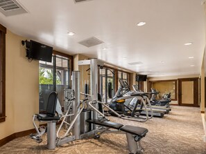 Un gimnasio con diferentes máquinas de ejercicio, un televisor de pantalla plana y amplios ventanales que permiten la entrada de luz natural.