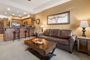 A modern living room with a leather sofa, a wooden coffee table, and a kitchen area in the background. - Crystal Peak Lodge 7008 ~ Ski-in/Ski-out ~ NEW LISTING ~ By CoralTree Residences (Breckenridge)