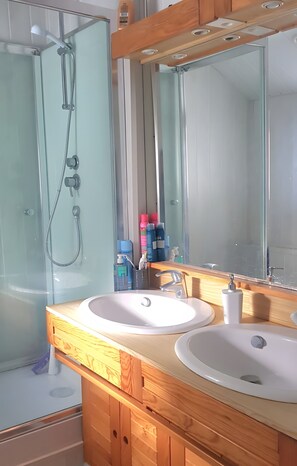 Une salle de bain avec une douche à parois de verre, deux lavabos et un grand miroir.