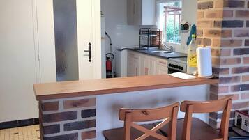 Eine Küche mit einer Holzausziehtheke, zwei Holzstühlen, einer weißen Tür und einer Ziegelwand.