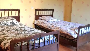 Une chambre avec deux lits en bois, chacun doté d’une tête de lit et d’un pied de lit, et recouverte d’une couvre-lit à motifs. Les murs sont d’une couleur jaune pâle, avec un motif discret.