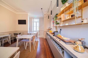 Een moderne keuken met witte kastjes, houten aanrecht en een bar. Er zijn meerdere zithoeken met tafels en stoelen, en een groot raam zorgt voor natuurlijk licht.