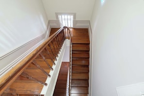 Un escalier en bois avec une rampe, des murs blancs et une petite fenêtre en haut.