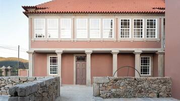 A two-story building with a red-tiled roof, stone walls, and a central door.