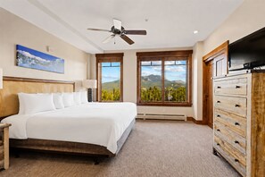 Ein Hotelzimmer mit einem großen Bett, einem Deckenventilator, einem Fernseher, einem Schminktisch und einem Fenster mit Blick auf die Berge.