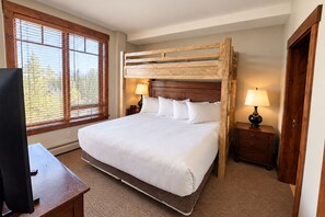 A hotel room with a large bed, wooden headboard, two bedside tables with lamps, a TV on a desk, and a window with blinds. - Crystal Peak Lodge 7204 ~ Ski-in/Ski-out ~ NEW LISTING ~ By CoralTree Residences (Breckenridge)