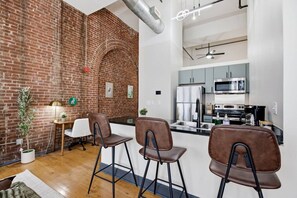 A modern kitchen with stainless steel appliances, a brick wall, and a dining area with bar stools. - Luxury Loft + King Bed Heart of Downtown STL (St. Louis)