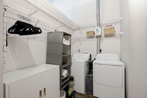 Une buanderie équipée de deux machines à laver, d’un étendoir, d’étagères où sont pliées les serviettes et d’une autre étagère où se trouve la lessive.