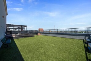 Une terrasse sur le toit, dotée d’un revêtement d’herbe artificielle, d’une pergola et offrant une vue sur le paysage urbain.