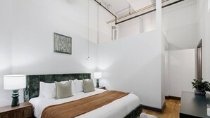 Ein modernes Hotelzimmer mit einem großen Bett, zwei Nachttischen, einem Schreibtisch, einem Stuhl, einem Spiegel und einer Topfpflanze.