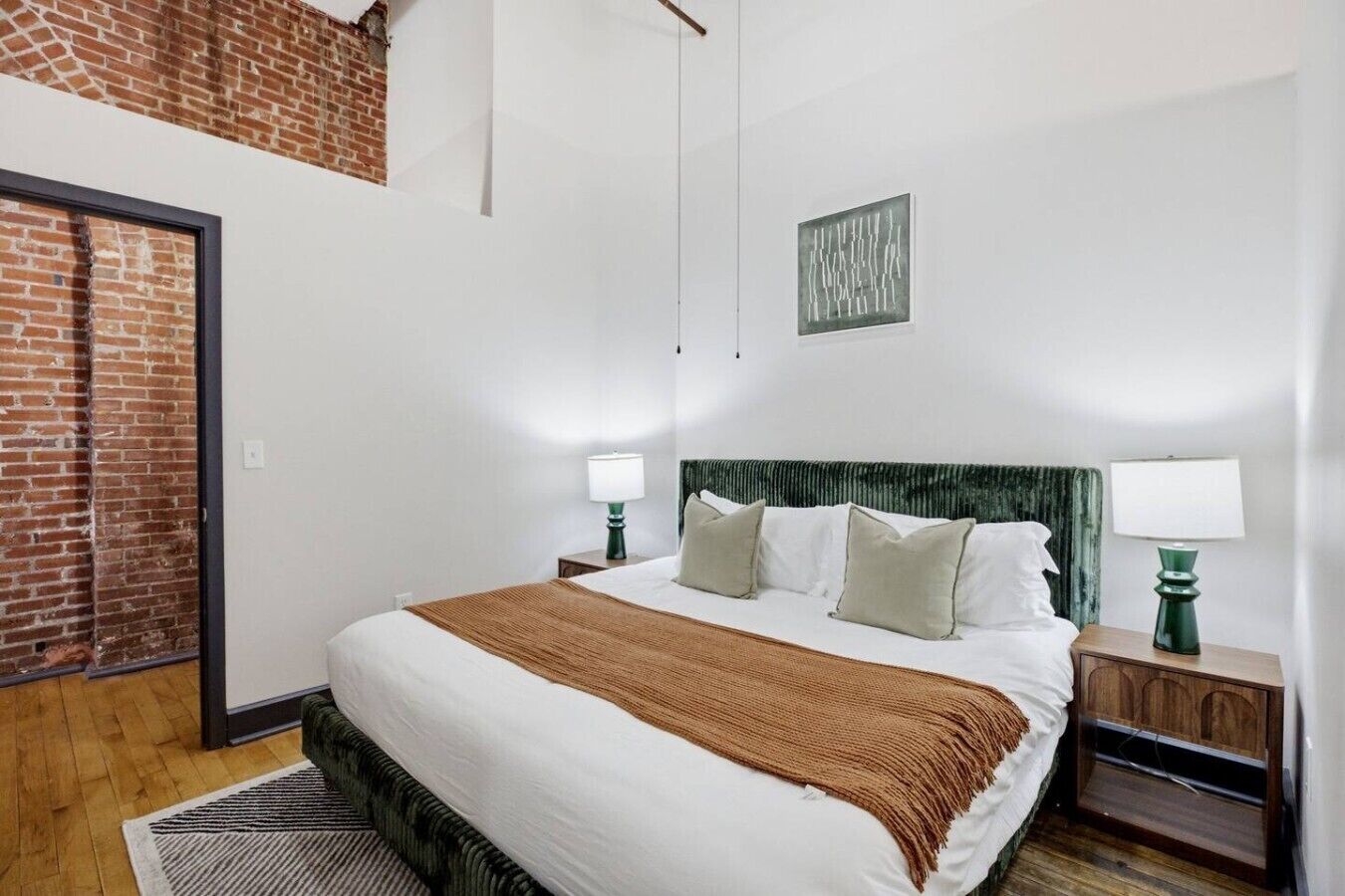 A hotel room with a large bed, two bedside tables with lamps, a brick wall, and a framed artwork on the wall.