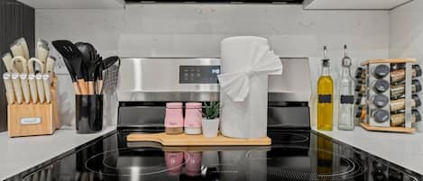 Una cocina moderna con estufa de acero inoxidable, un juego de cuchillos, saleros y pimenteros, una toalla y un especiero.