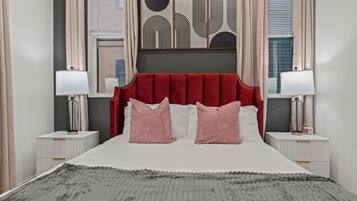 A bedroom with a red upholstered headboard, two bedside tables with lamps, a grey textured rug, and abstract wall art.