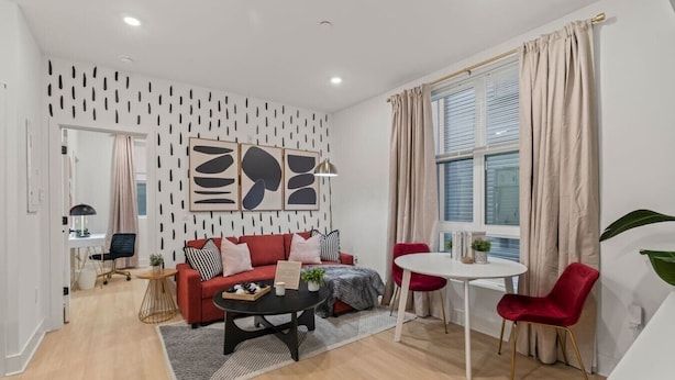 Ein modernes Wohnzimmer mit einem roten Sofa, einem Couchtisch und einem Essbereich mit einem weißen Tisch und roten Stühlen.