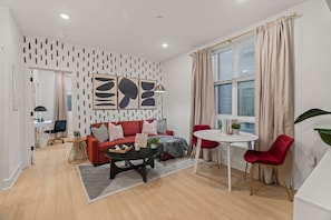 A modern living room with a red sofa, a coffee table, and a dining area with a white table and red chairs. - 1BR | Art Museum, UPenn, University City, & Zoo (Philadelphia)