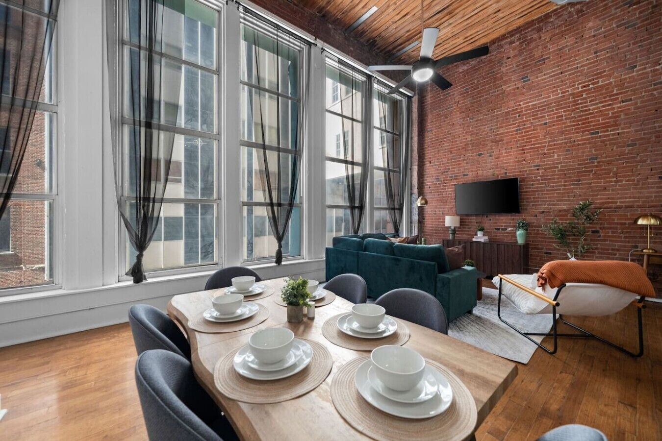 Un espace repas avec un mur en briques, de grandes fenêtres et un ventilateur de plafond.
