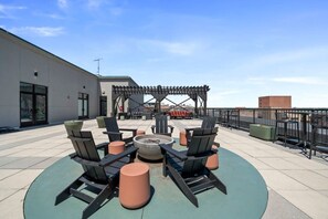 Eine Dachterrasse mit Sitzgelegenheiten im Freien, einer Feuerstelle und einer Pergola.