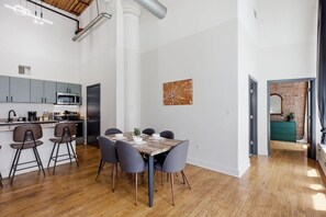 A modern kitchen with a dining area, wooden flooring, and a brick wall.