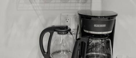 A kitchen counter with a coffee maker, a glass carafe, and a set of white mugs on a shelf.