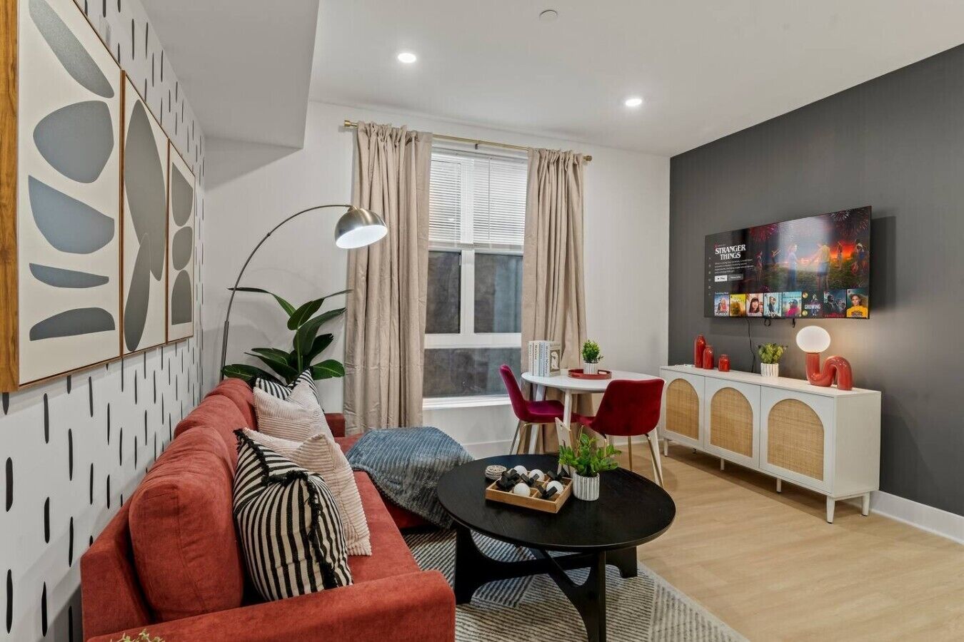 A modern living room with a sofa, a dining table with chairs, a TV mounted on the wall, and a cabinet with decorative items.