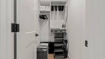 A narrow hallway with a closet containing folded clothes, a hanging rack, and a small shelf with a kettle.