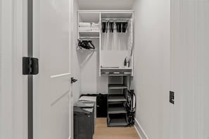 A narrow hallway with a closet containing folded clothes, a hanging rack, and a small shelf with a kettle. - University City 1BR | Zoo, UPenn & Museums (Philadelphia)