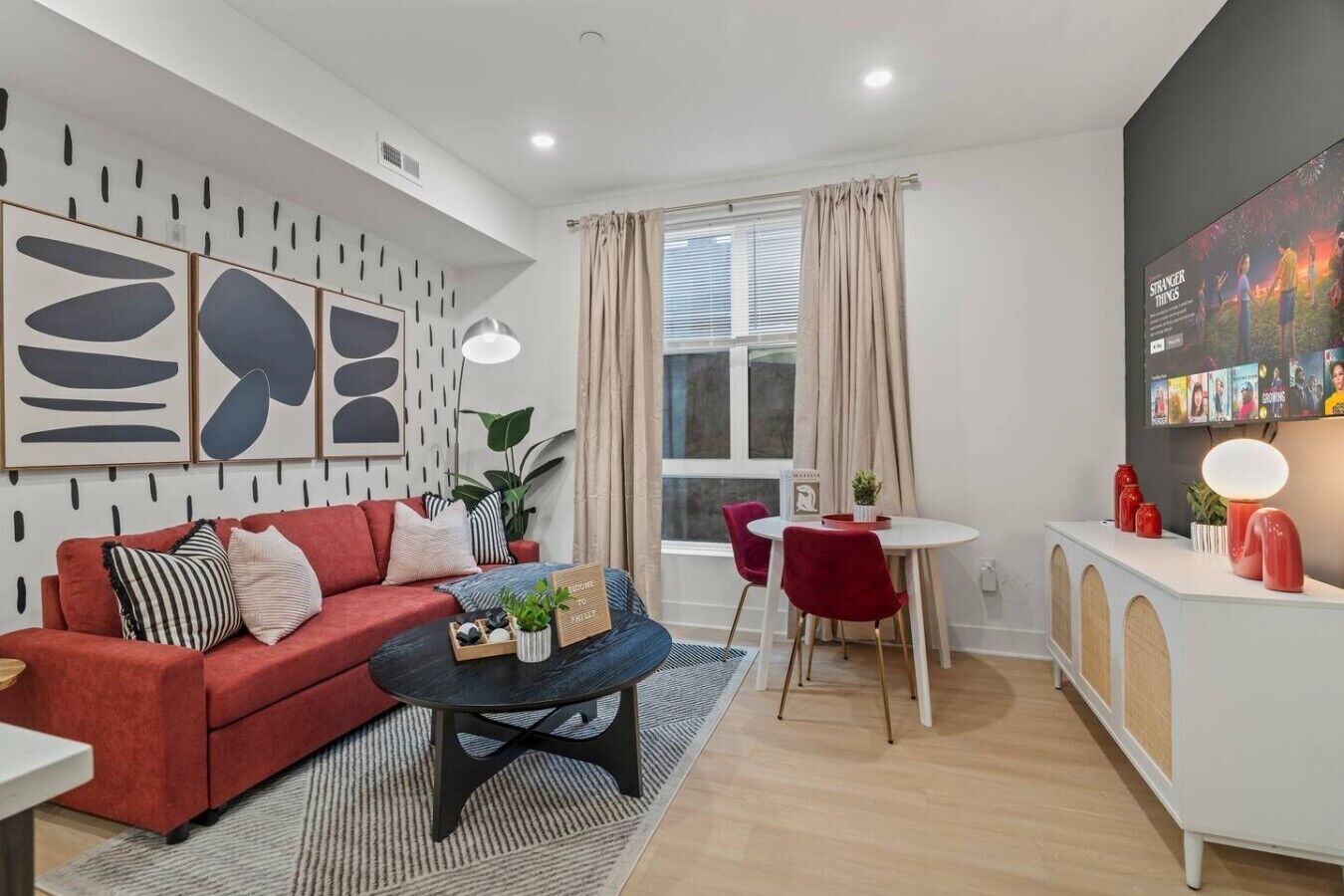 A modern living room with a red sofa, a coffee table, and a dining area with a white table and red chairs.