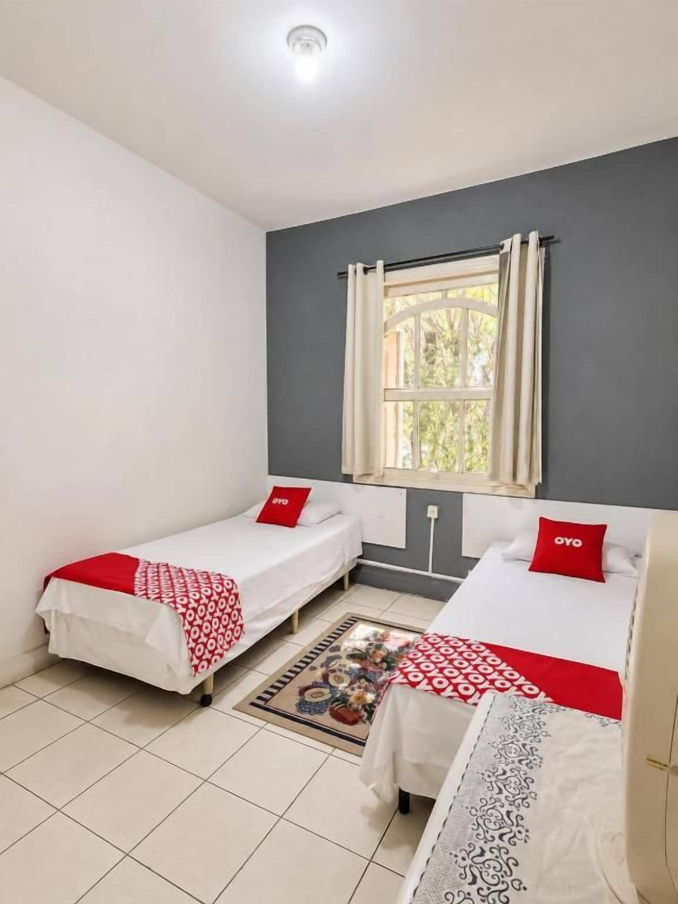 A room with two beds, a window with curtains, and a tiled floor.