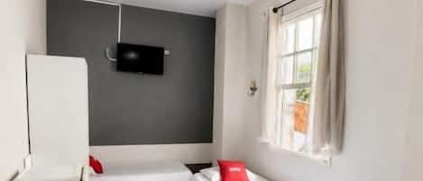 Una habitación pequeña y limpia con cama, escritorio, silla, ventilador de techo y ventana con cortinas.