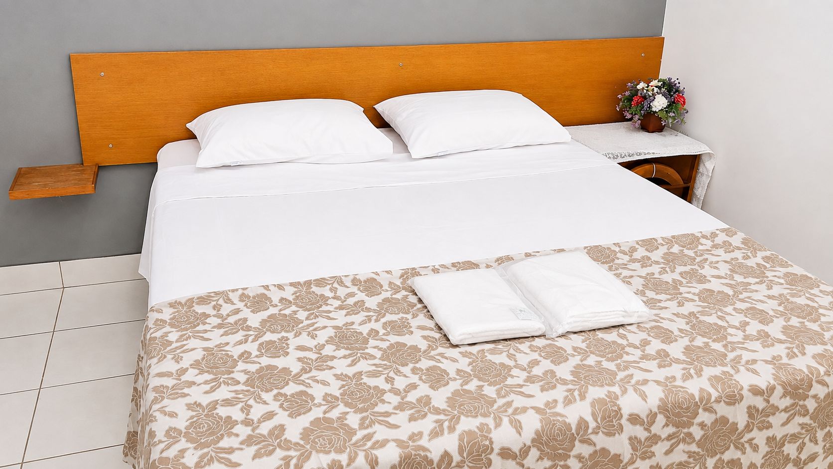 A neatly made bed with a wooden headboard, white bedding, and a floral-patterned bedspread.