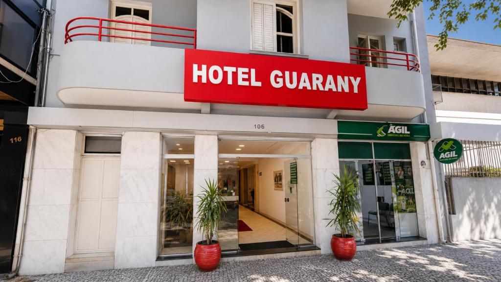 A hotel named 'HOTEL GUARANY' with a red sign, a green 'AGIL' sign, and a number '106' on the facade.