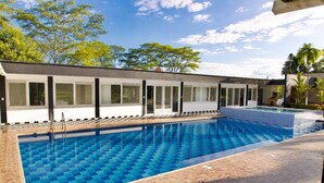 A swimming pool with a checkered pattern, surrounded by a building with large windows and a tiled deck.