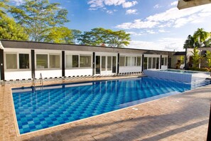 Piscina com padrão quadriculado, cercada por um edifício com grandes janelas e um deck revestido com azulejos.