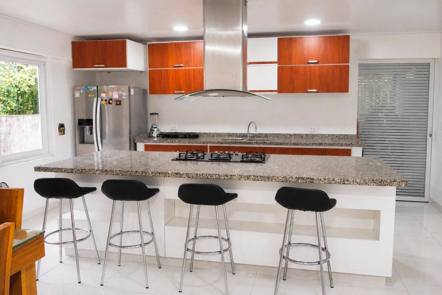 Een moderne keuken met een centraal eiland, barstoelen, roestvrijstalen apparatuur en houten keukenkastjes.