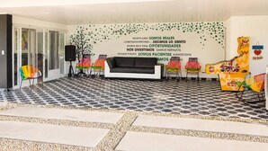 A waiting area with a black and white patterned floor, a black sofa, colorful chairs, and a wall with motivational text in Spanish.