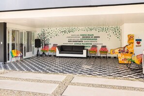 Uma área de espera com piso em padrão preto e branco, um sofá preto, cadeiras coloridas e uma parede com texto motivacional em espanhol.