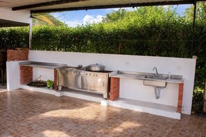 Cozinha externa com bancada de aço inoxidável, pia e forno de tijolos.