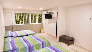 A hotel room with two beds, a small table, a TV mounted on the wall, and a window with blinds.